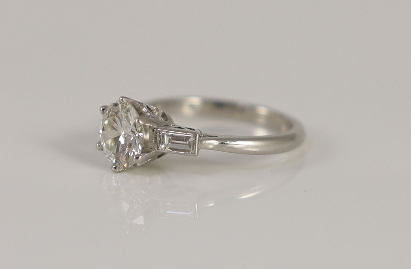 A platinum and single stone diamond ring, with baguette cut diamond set shoulders